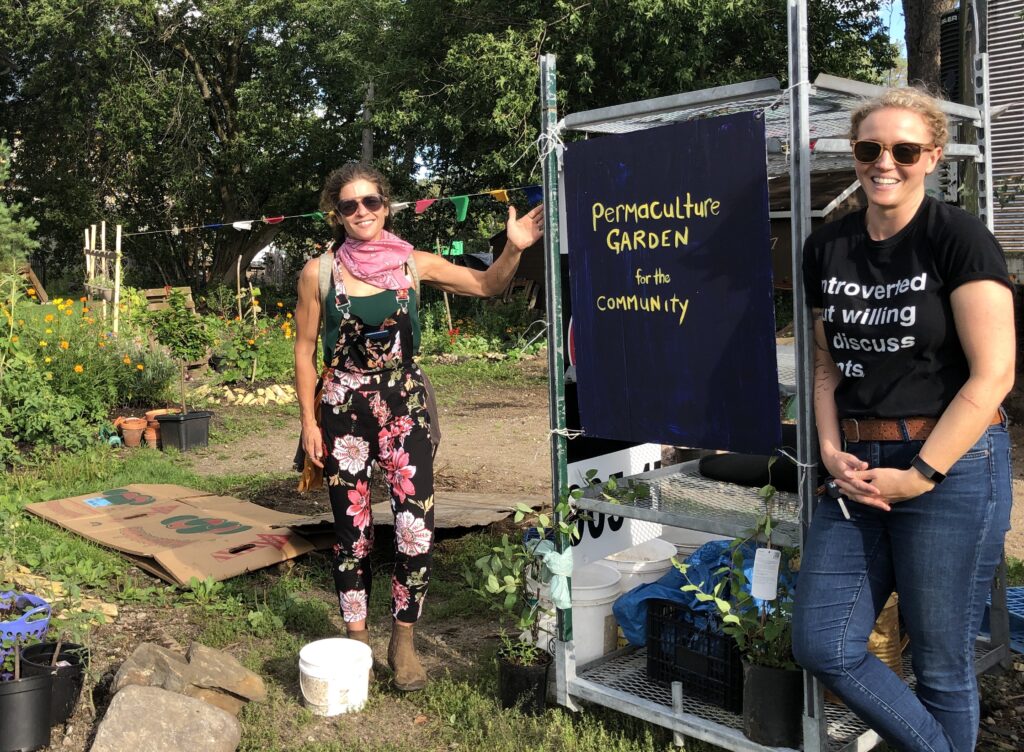 Picture of Tricia Bilissis and Bet Smith with a sign that says "Permaculture Garden for the Community." 