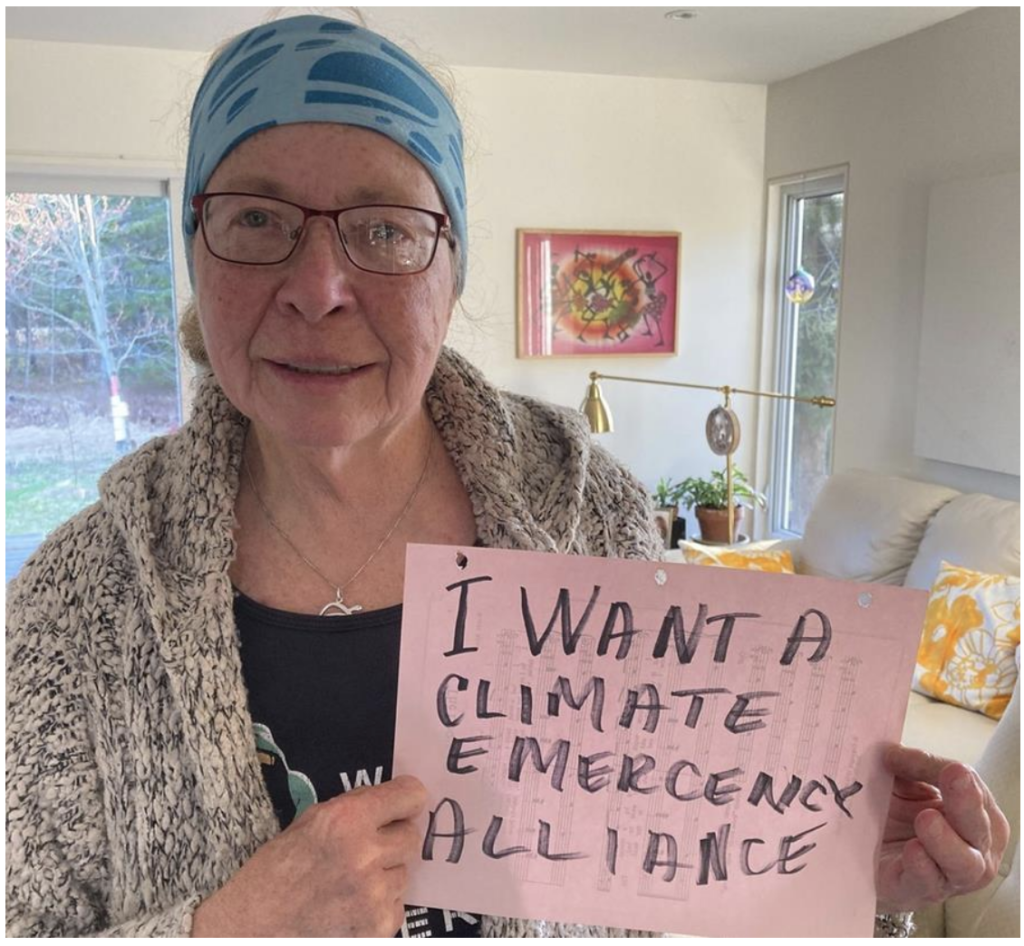 Picture of Sue McKenzie with sign reading "I want a climate emergency alliance"